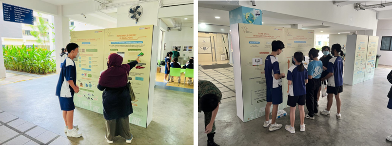 Students in school uniforms view educational display boards about renewable energy in an indoor exhibition.