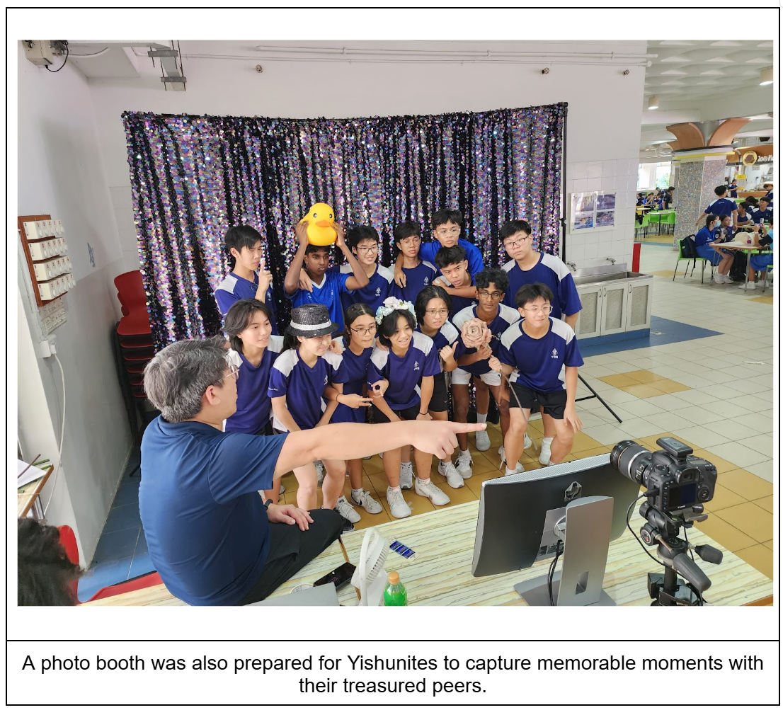 Students in blue uniforms pose at a photo booth with a sequin backdrop while an adult points at a monitor.