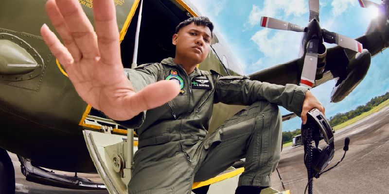 Aircrew in a flight suit with his hand extended, standing in front of a helicopter.