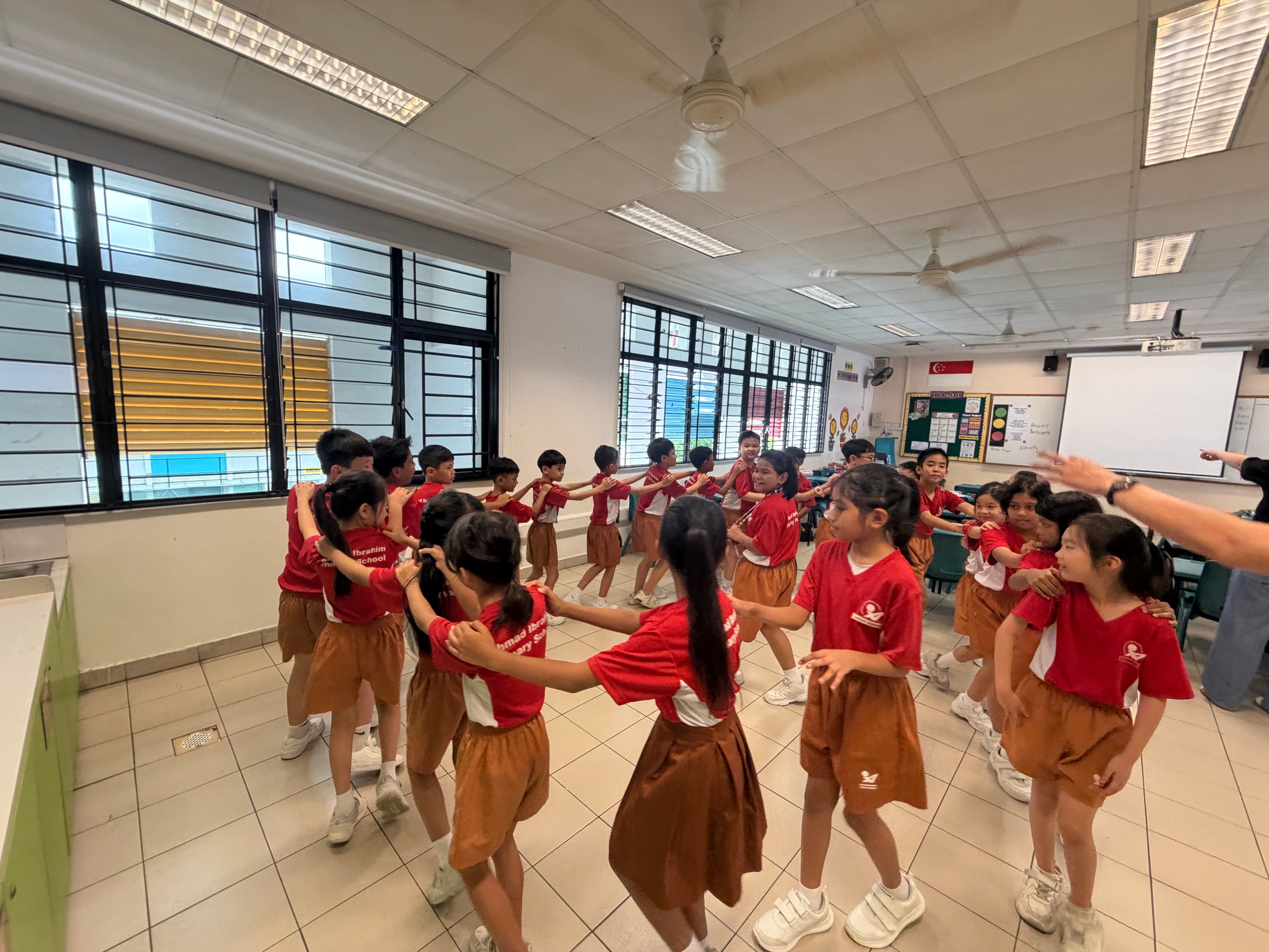 Students take part in a classroom teamwork activity with hands on classmates' shoulders.