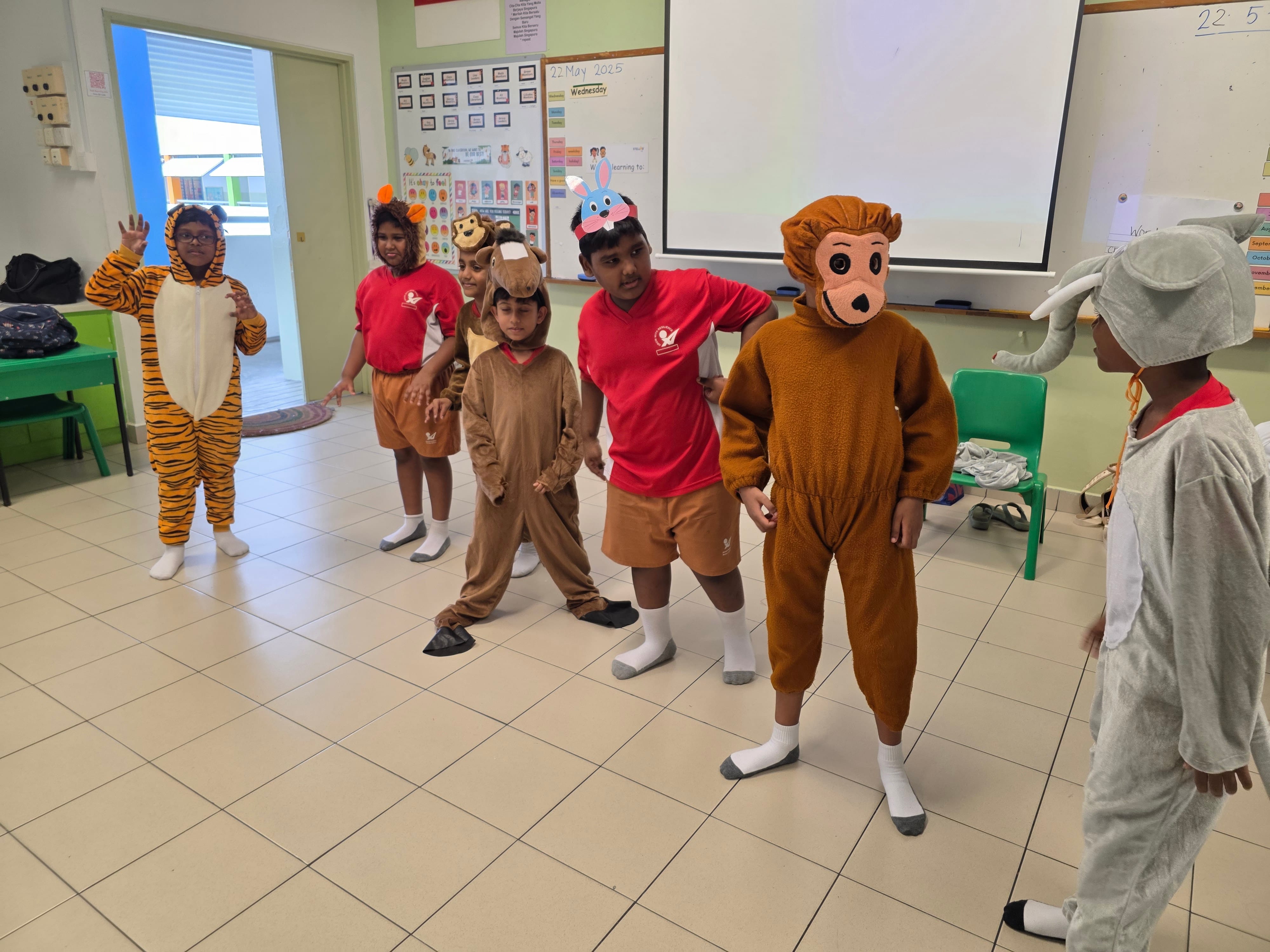 Children in a classroom wearing animal costumes including tiger, monkey, camel, and elephant for a school performance.