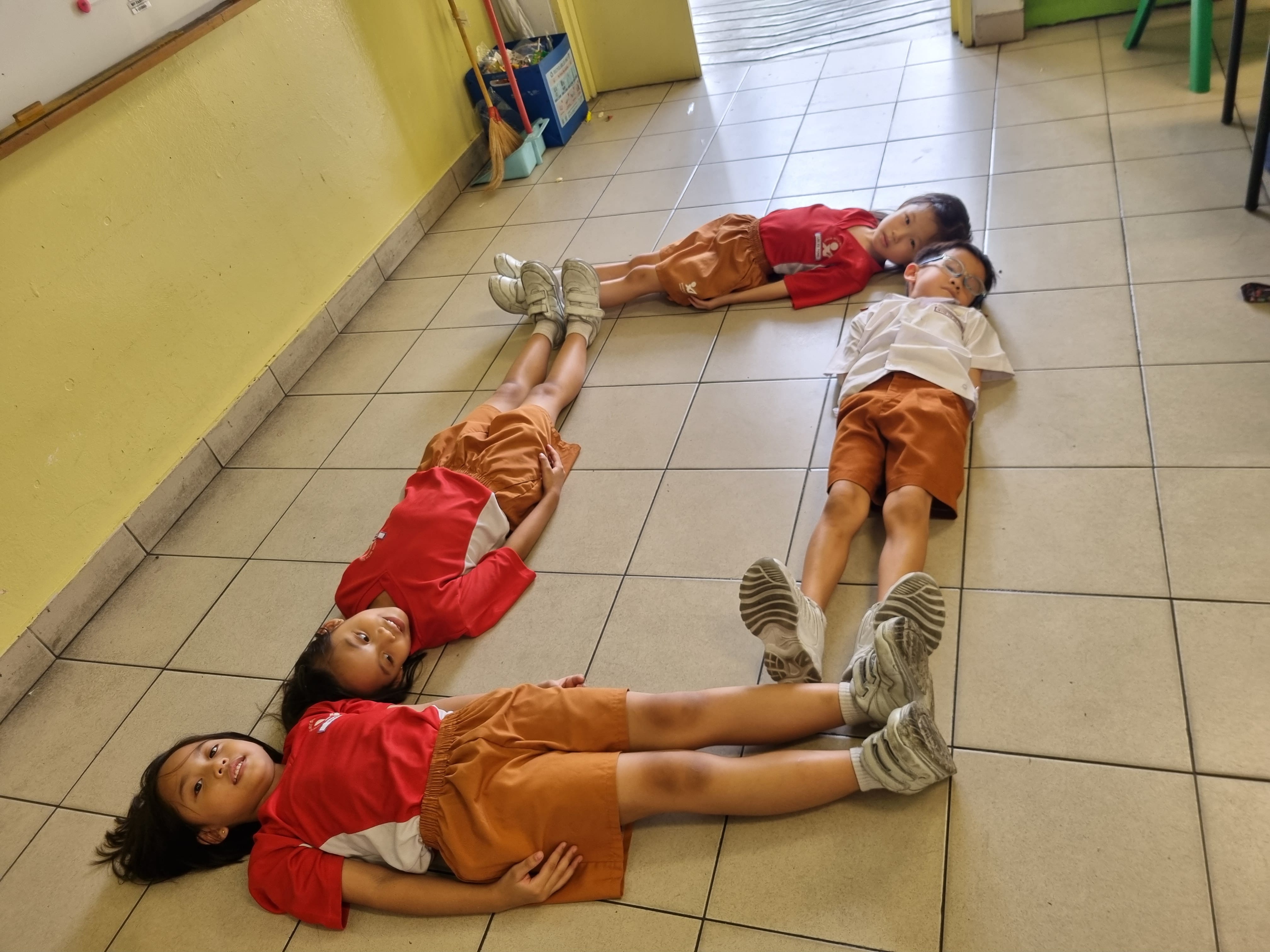 Students lie on the classroom floor during a drama lesson activity.