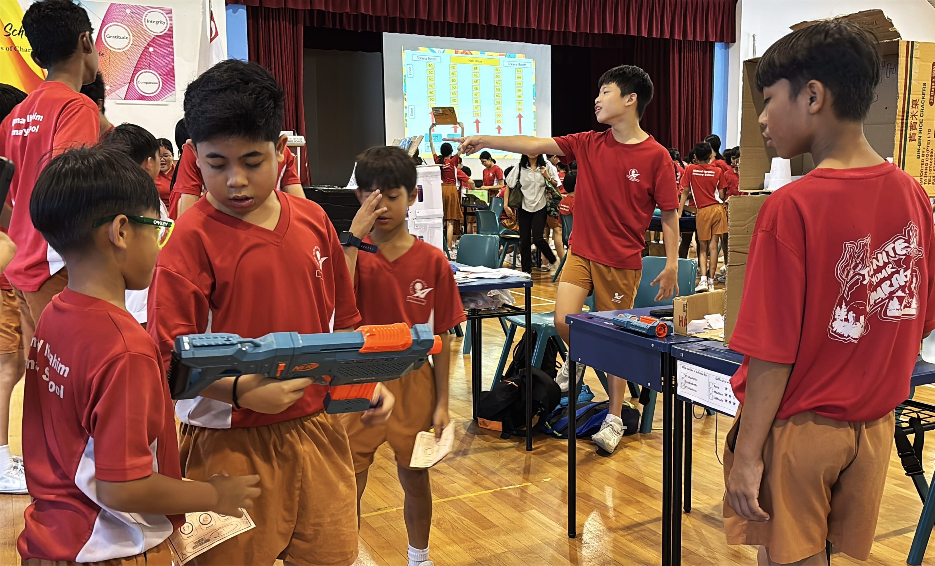 Students in red uniforms stand in a school hall, one boy holding a Nerf blaster while another points directions.