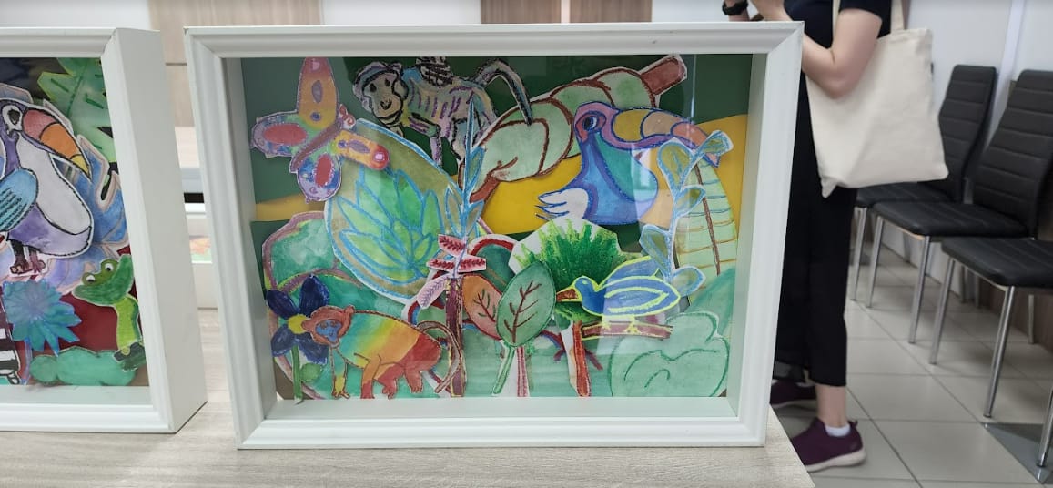 Framed children's artwork showing colorful jungle animals, birds, butterfly, and plants on a green background.