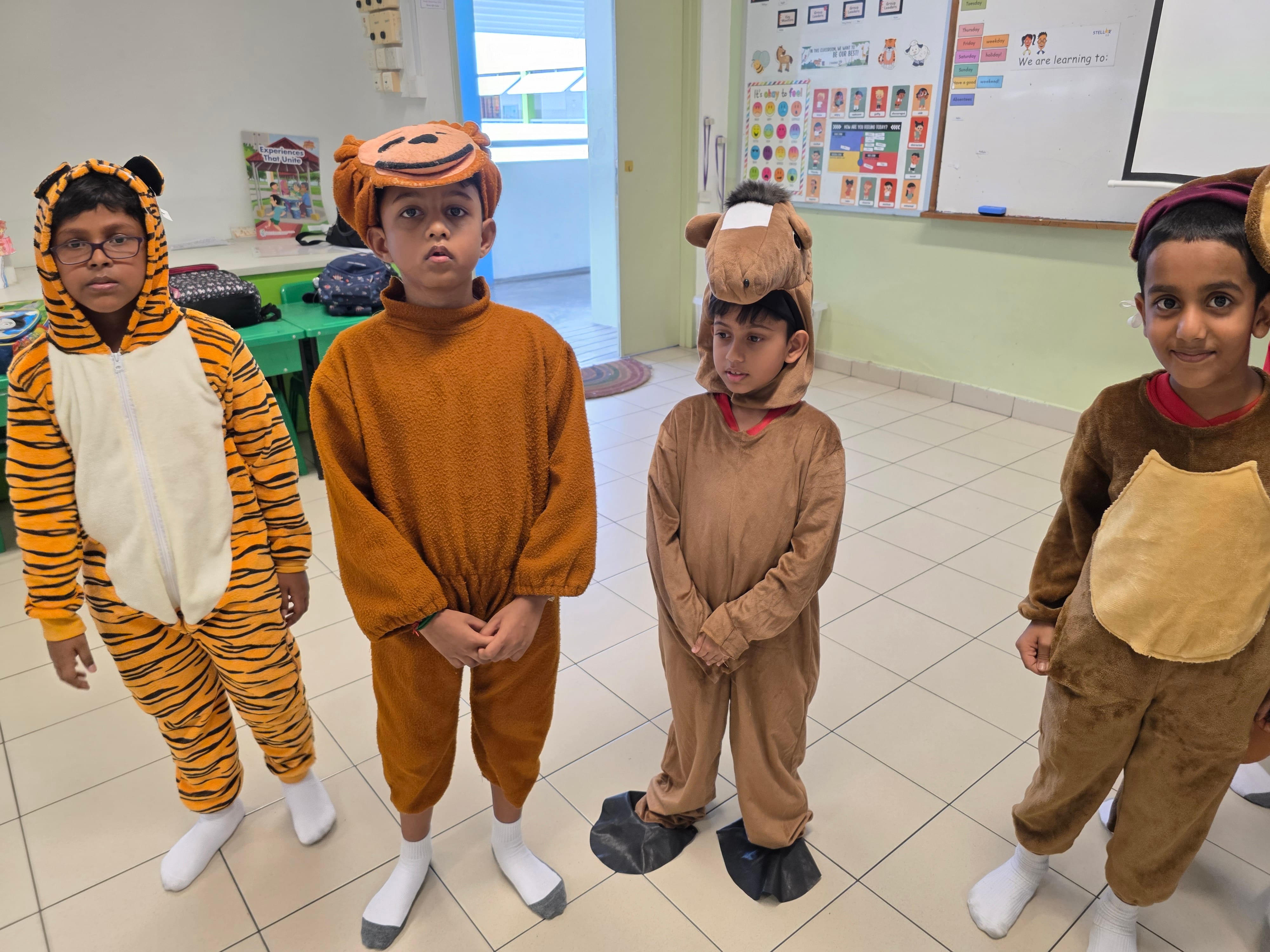 Four children stand in a classroom wearing animal costumes including a tiger, monkey, camel, and bear.