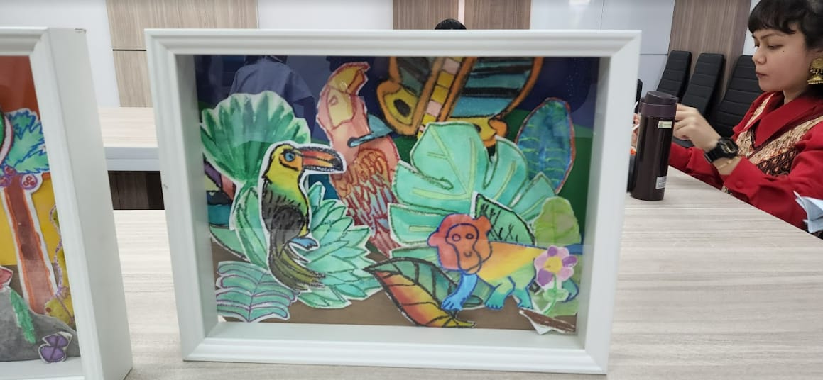 White framed colorful artwork showing a toucan, monkey, and tropical leaves, displayed on a table near a seated woman.