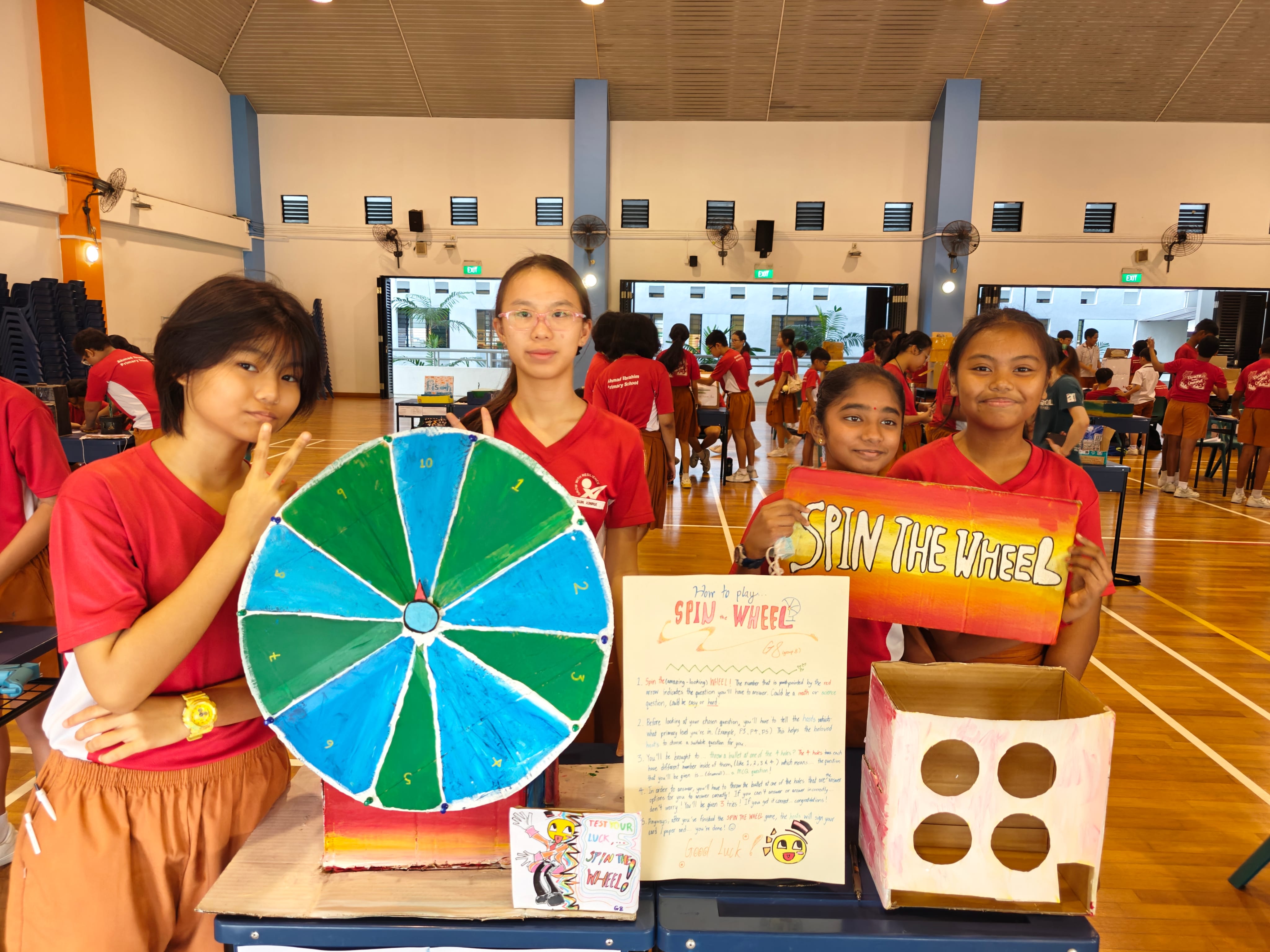 Students showcase a handmade spin-the-wheel game at a school activity fair.