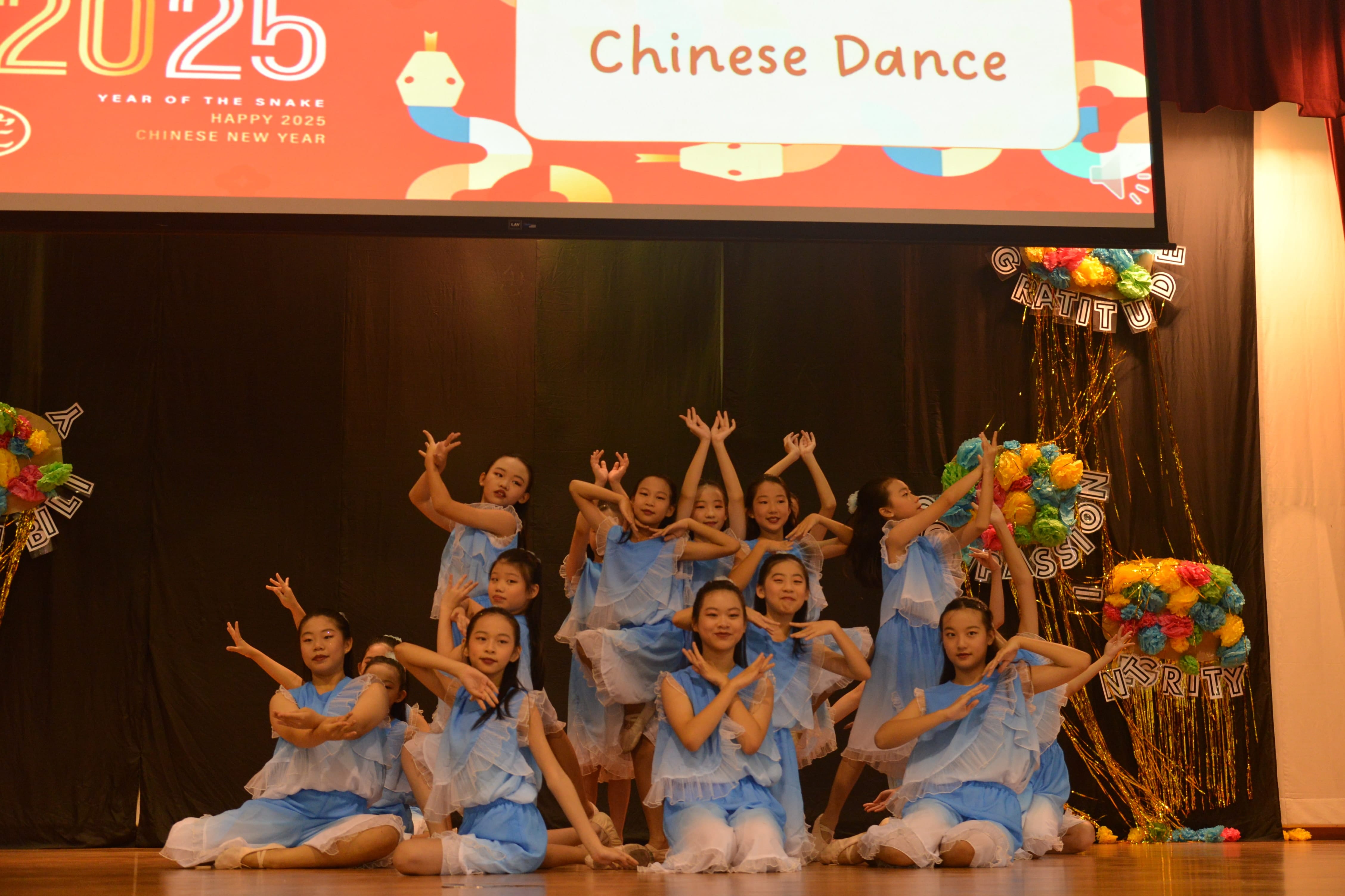 Girls in blue costumes perform a Chinese dance on stage at a 2025 Chinese New Year celebration.