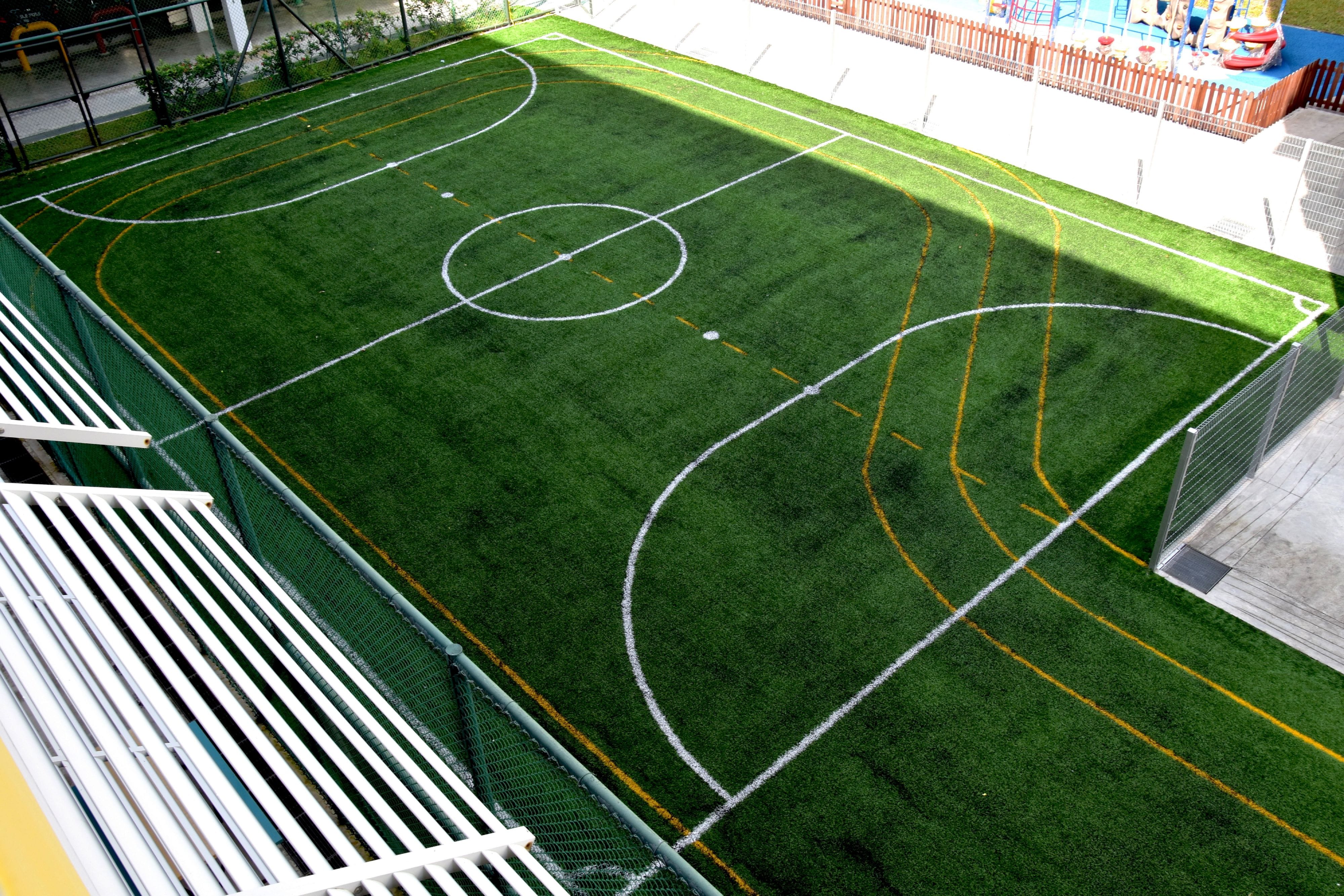 Aerial view of an artificial turf sports field with white and yellow painted lines, fenced on the sides.