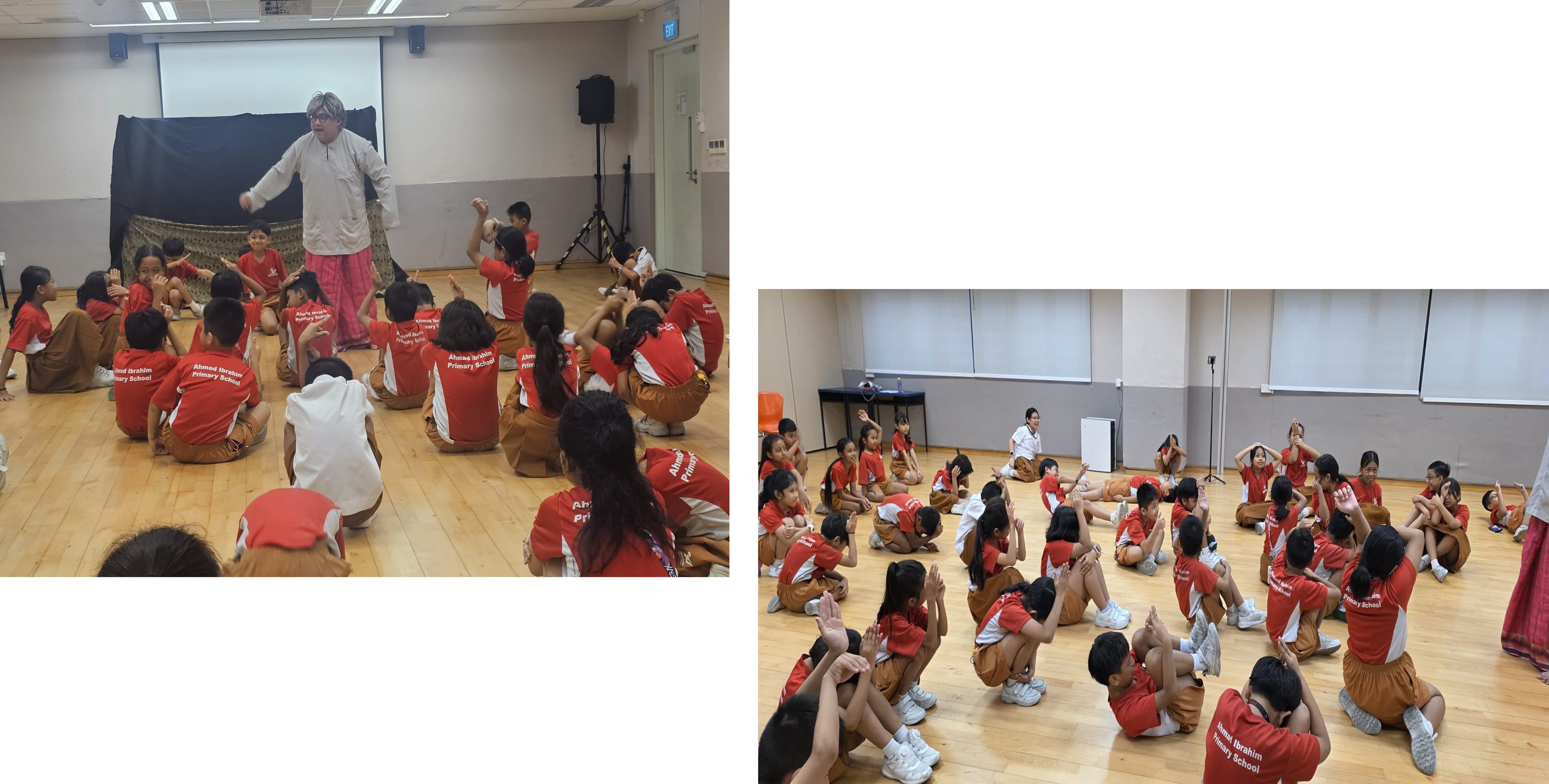 Primary school children in red uniforms sit on a hall floor doing hand gestures led by an adult performer.
