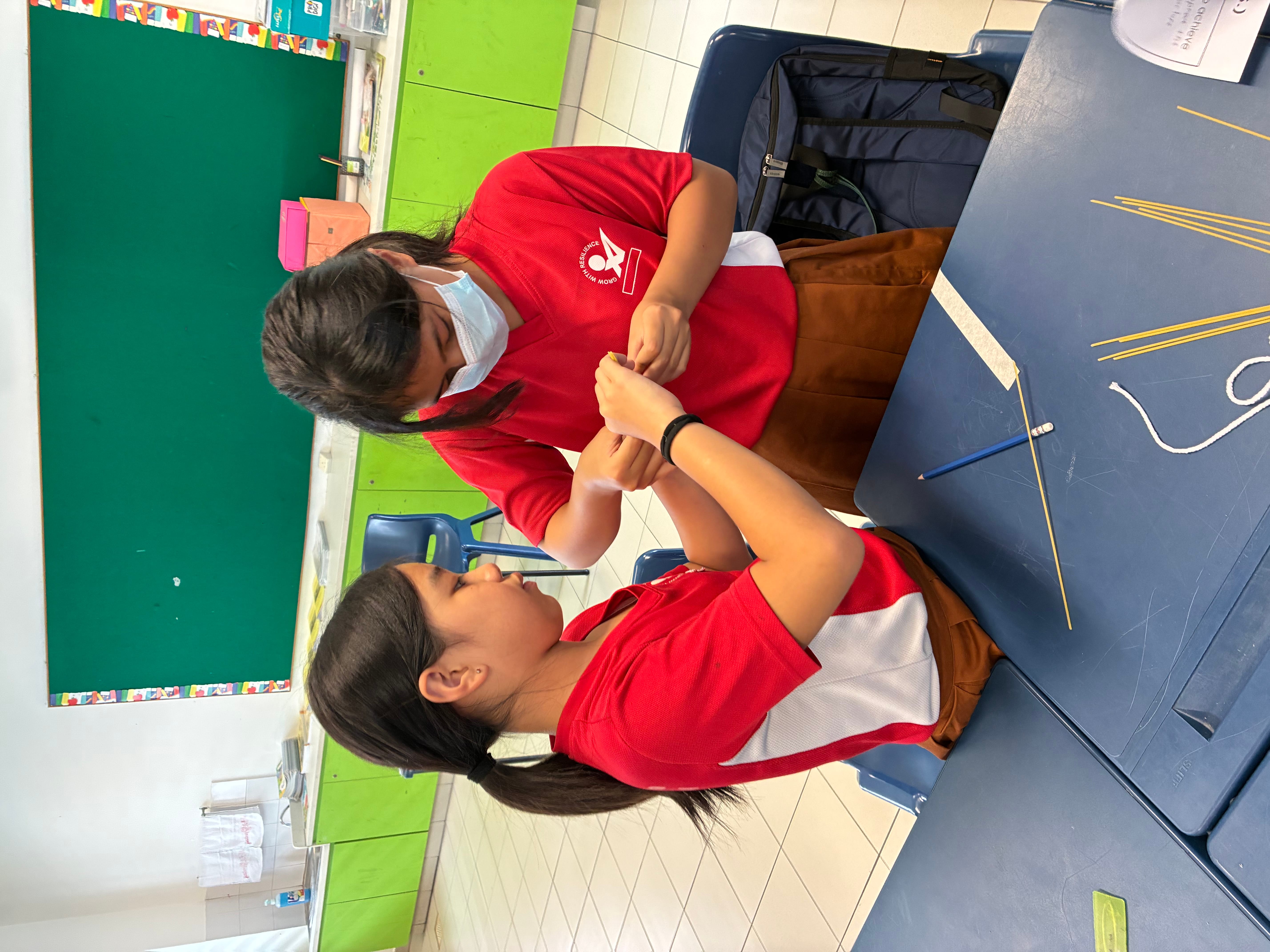 Two students build a structure with spaghetti and marshmallows during a classroom activity.