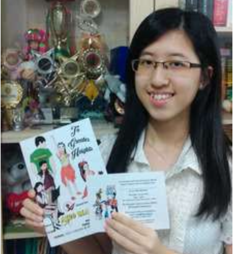 Smiling woman with glasses holds an open illustrated booklet, with trophies and books on shelves behind.