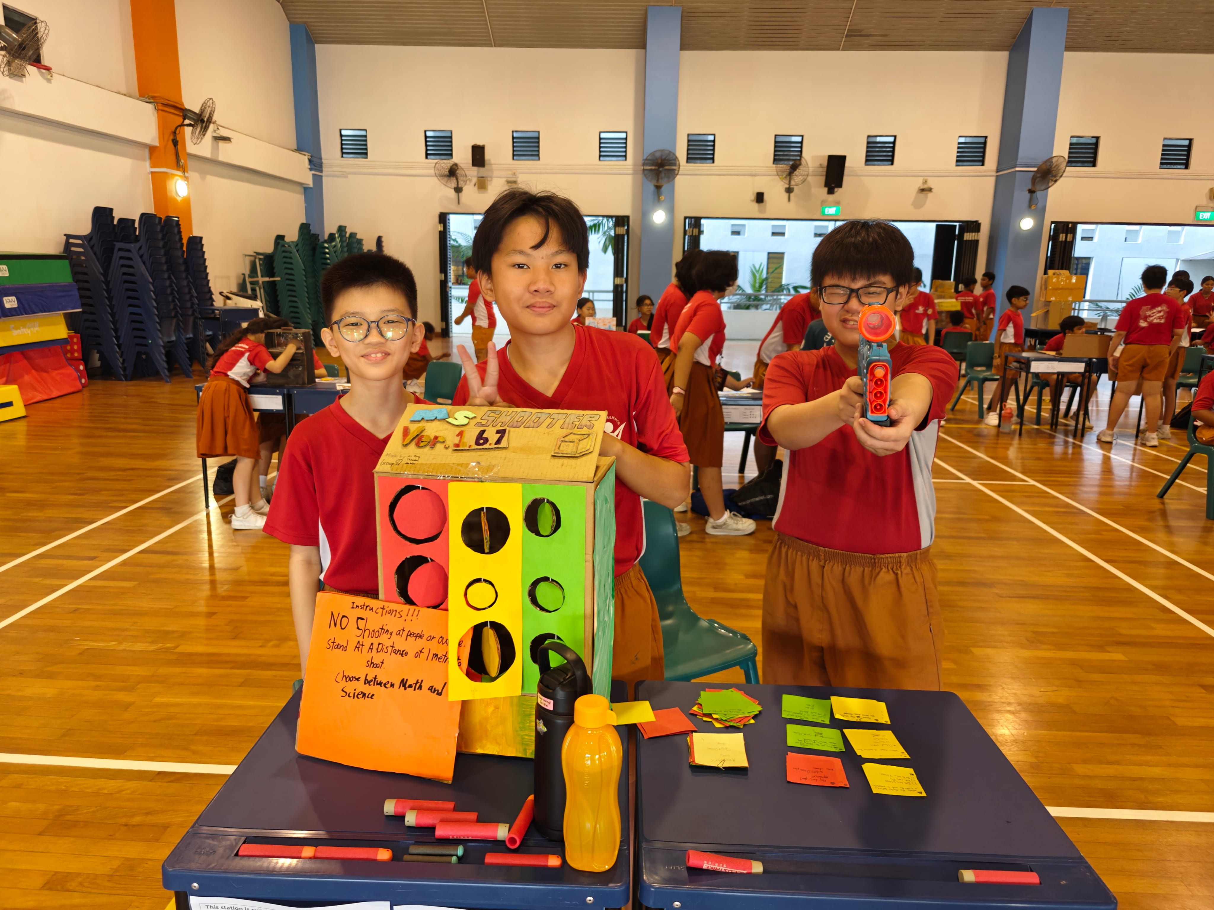 Students present a handmade target shooting game at a school activity fair.