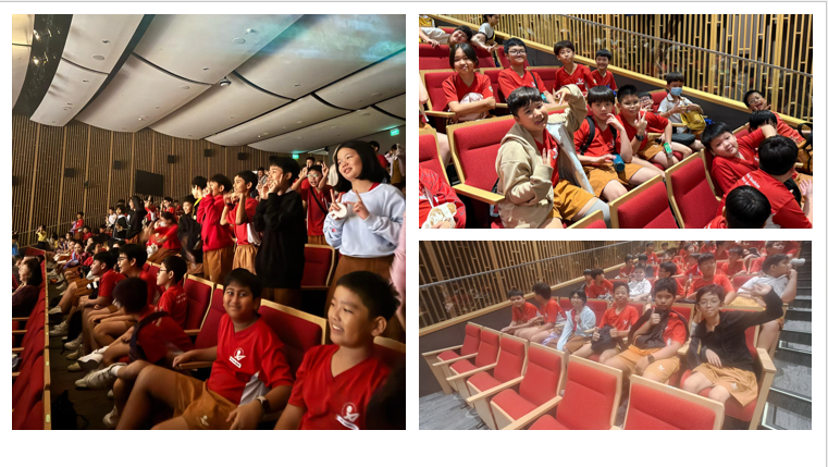 Students in red shirts sitting and standing in a theater with red seats, smiling and gesturing.