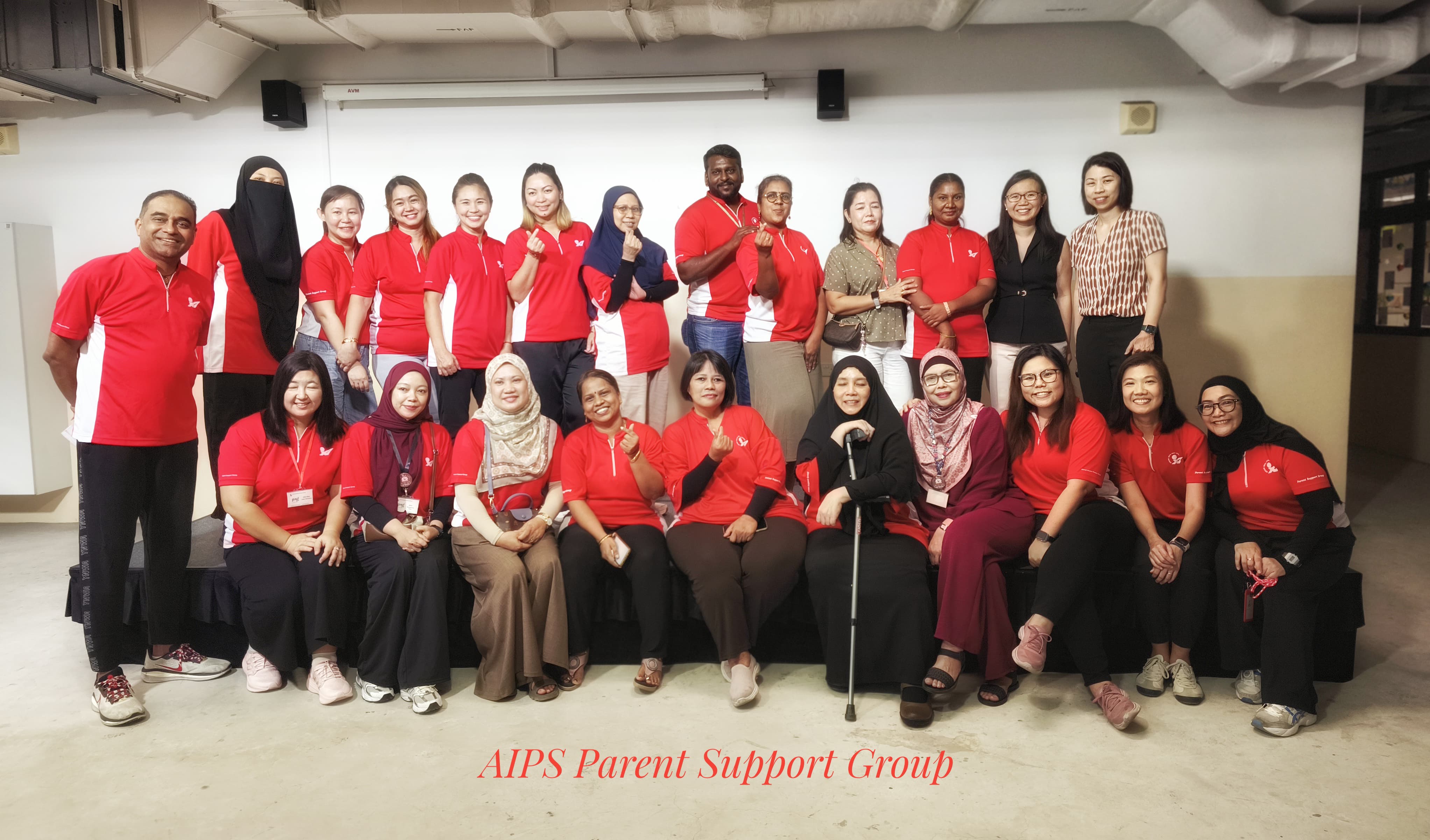 A large group of adults posing indoors, most wearing matching red polo shirts, labeled AIPS Parent Support Group.