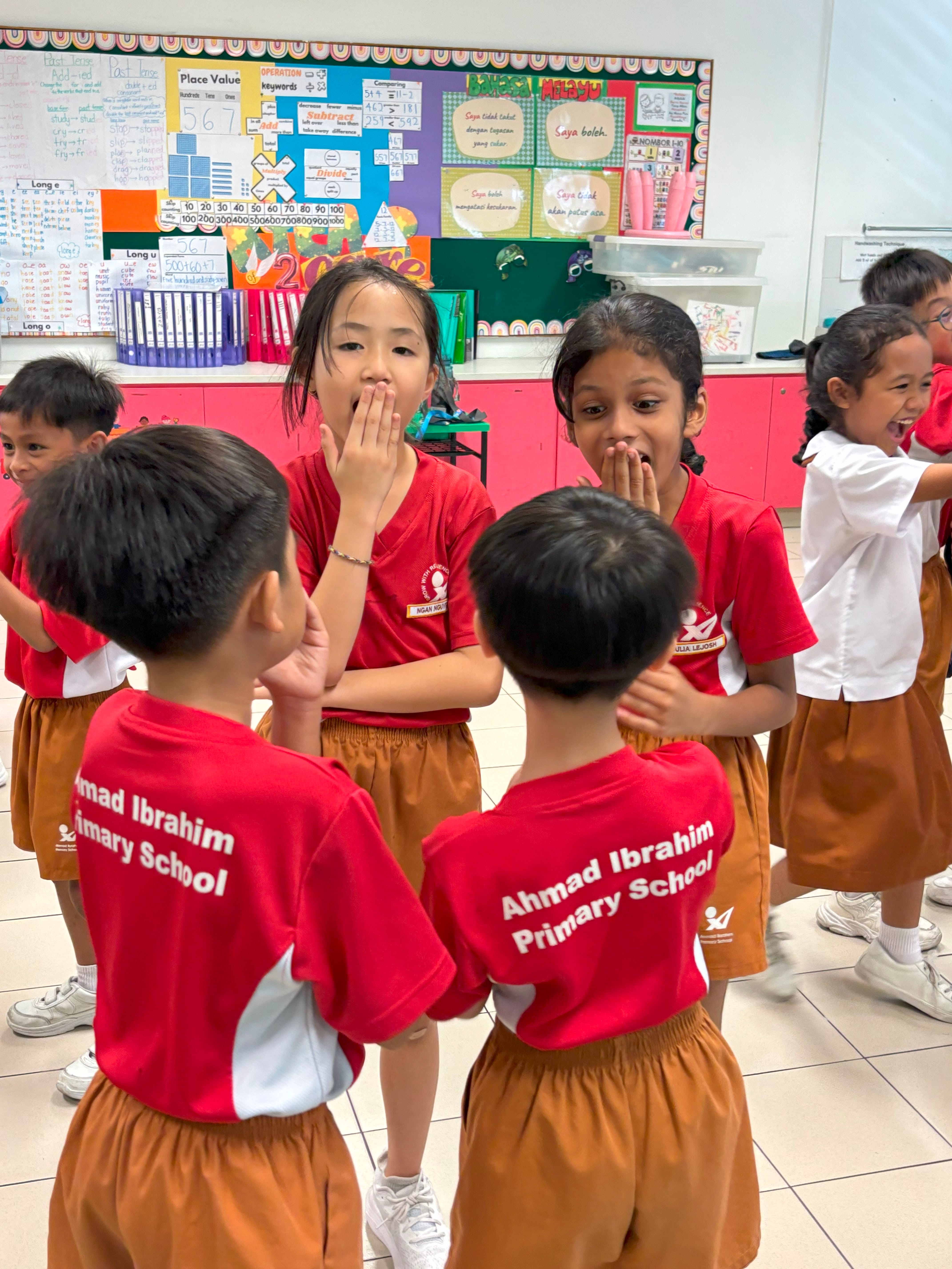 Students act out a classroom drama activity with expressive facial reactions.