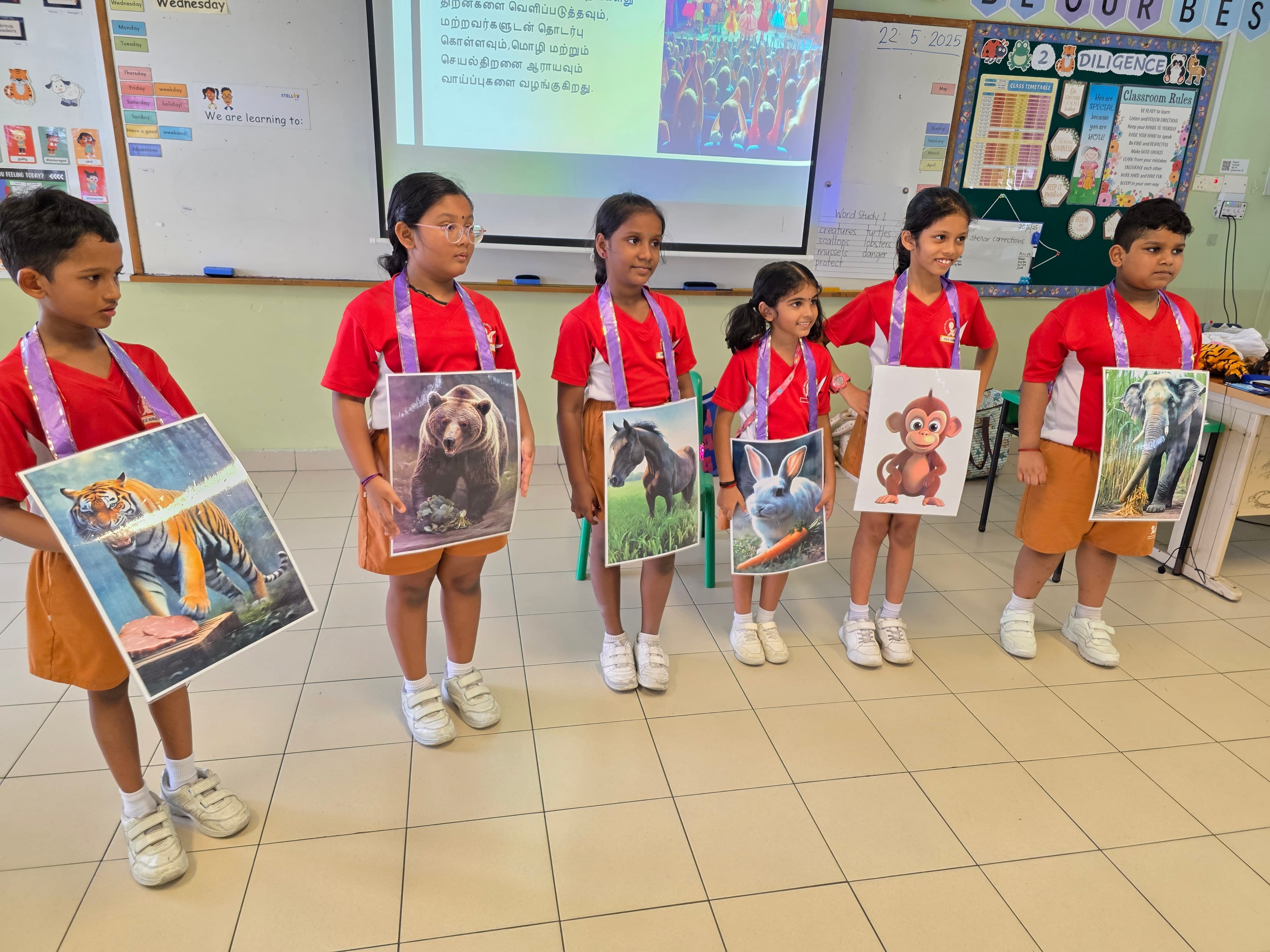 Six children in red school uniforms stand in a classroom holding large animal posters including a tiger, bear, horse, rabbit, monkey, and elephant.