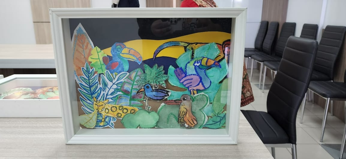 A white framed artwork showing colorful painted birds and tropical leaves on a table near black chairs.