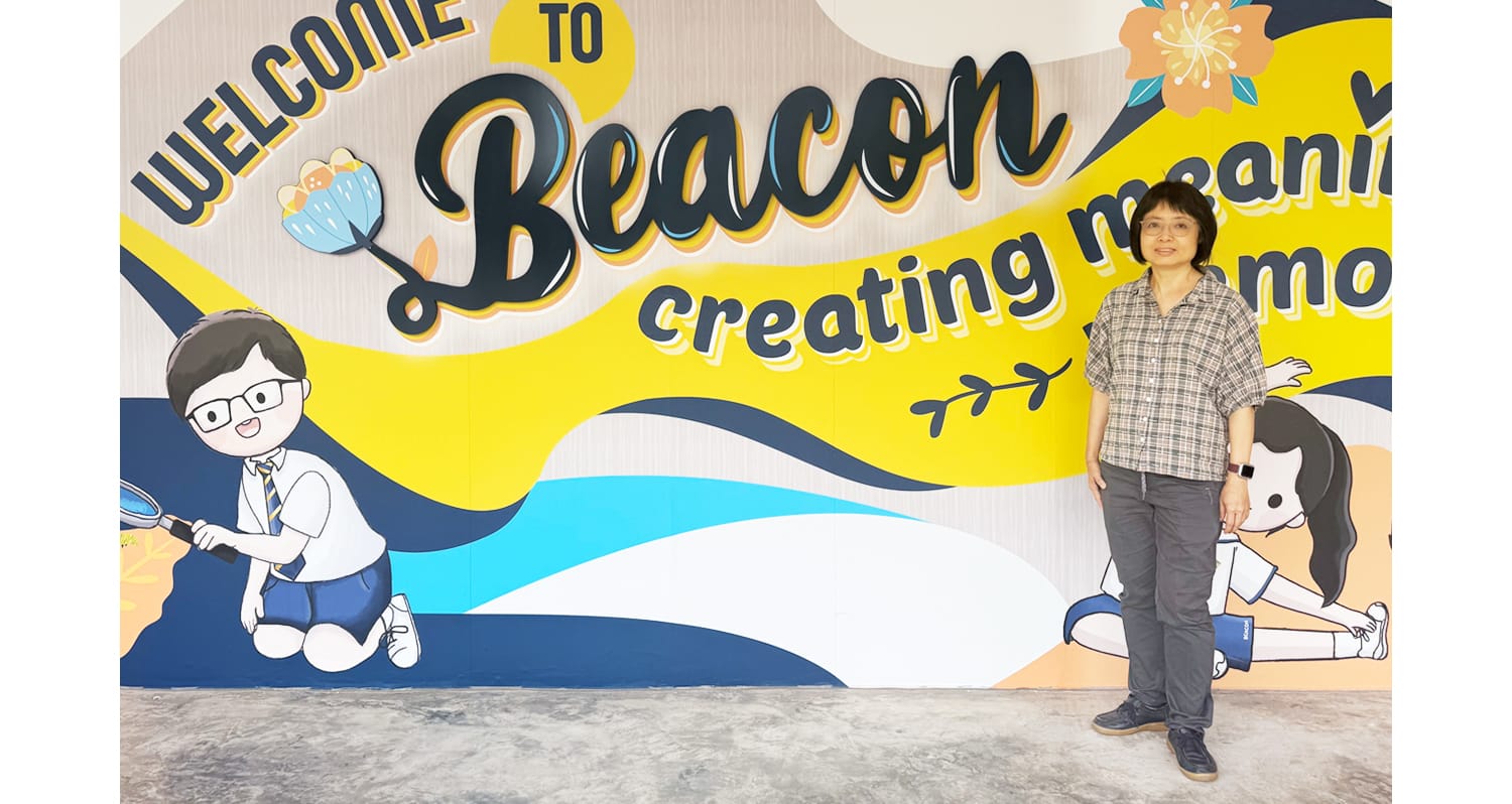 A woman in a plaid shirt stands before a colorful mural reading "Welcome to Beacon, creating meaning."