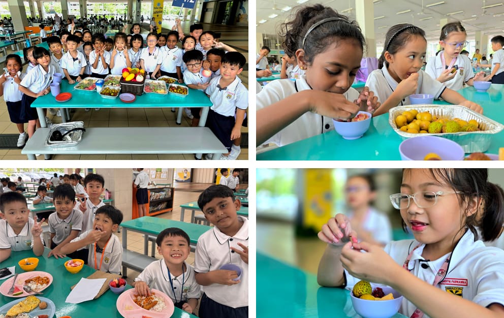 Young school children in uniforms eating and posing with food trays and fruit at cafeteria tables.