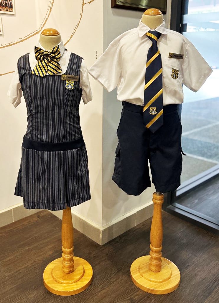 Two child mannequins display school uniforms: a striped pinafore with yellow-black bow tie, and white shirt with navy shorts and striped tie.