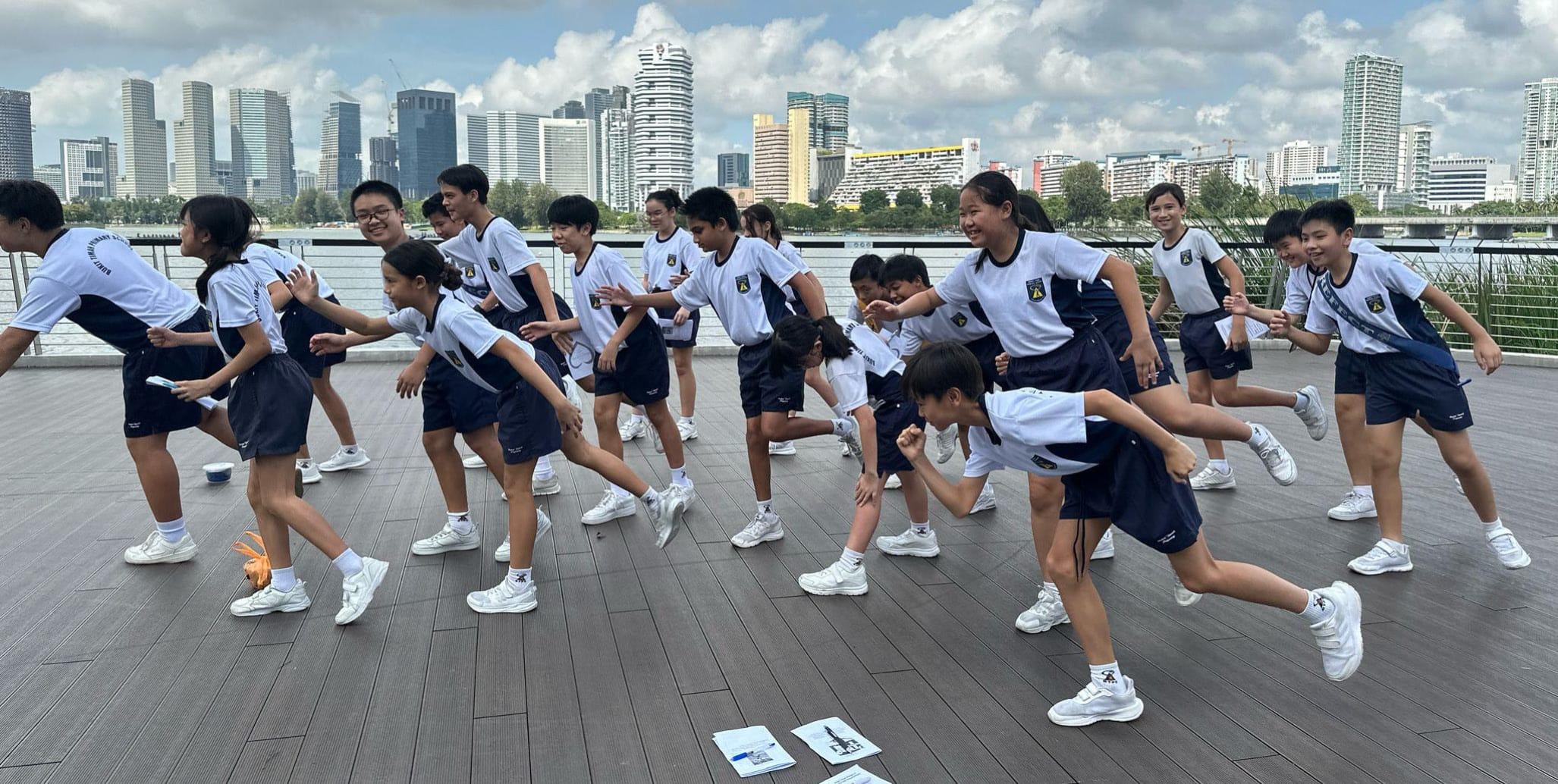 Students run in formation during a team-building activity on a waterfront promenade.