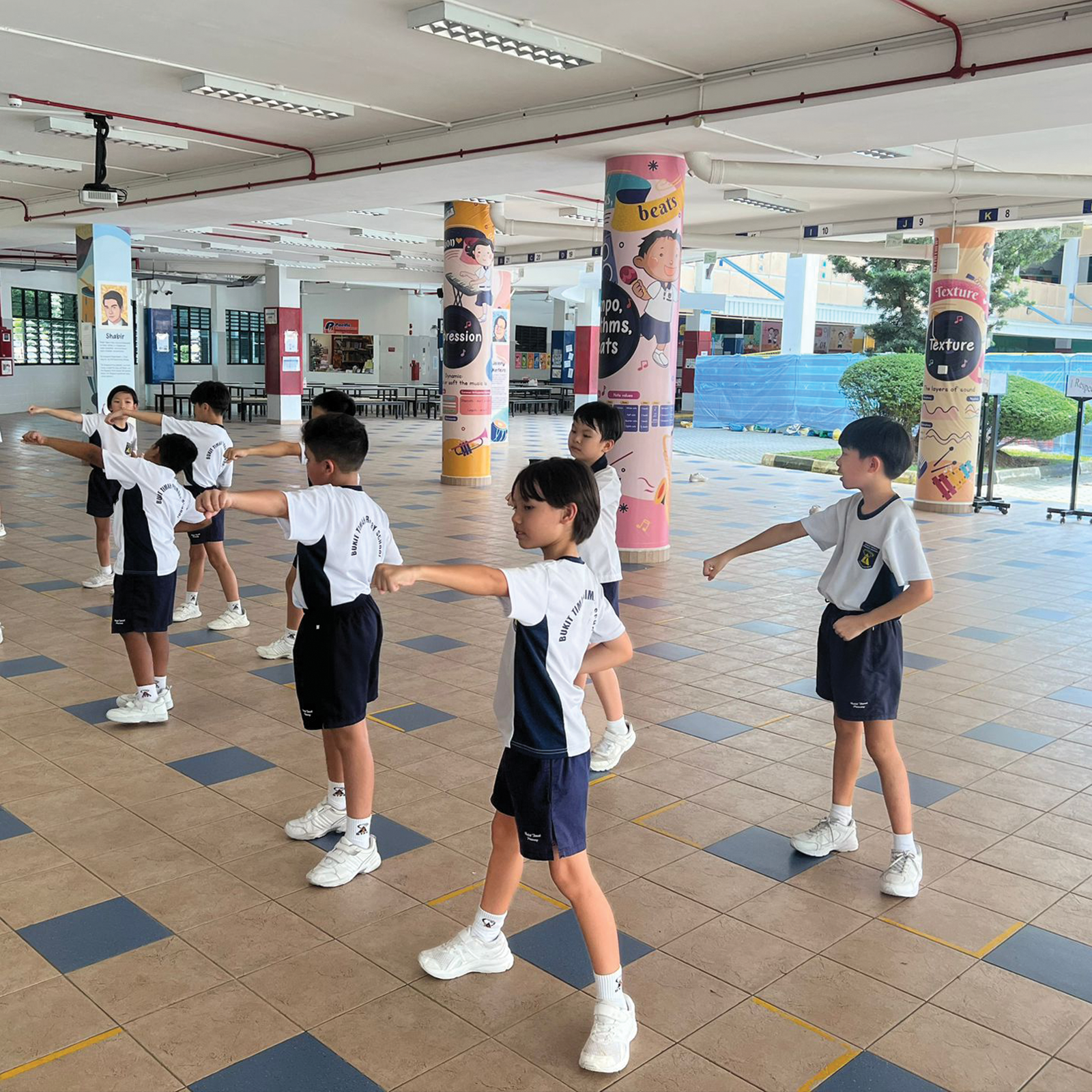 Students practise wushu punching techniques in formation in a school plaza.