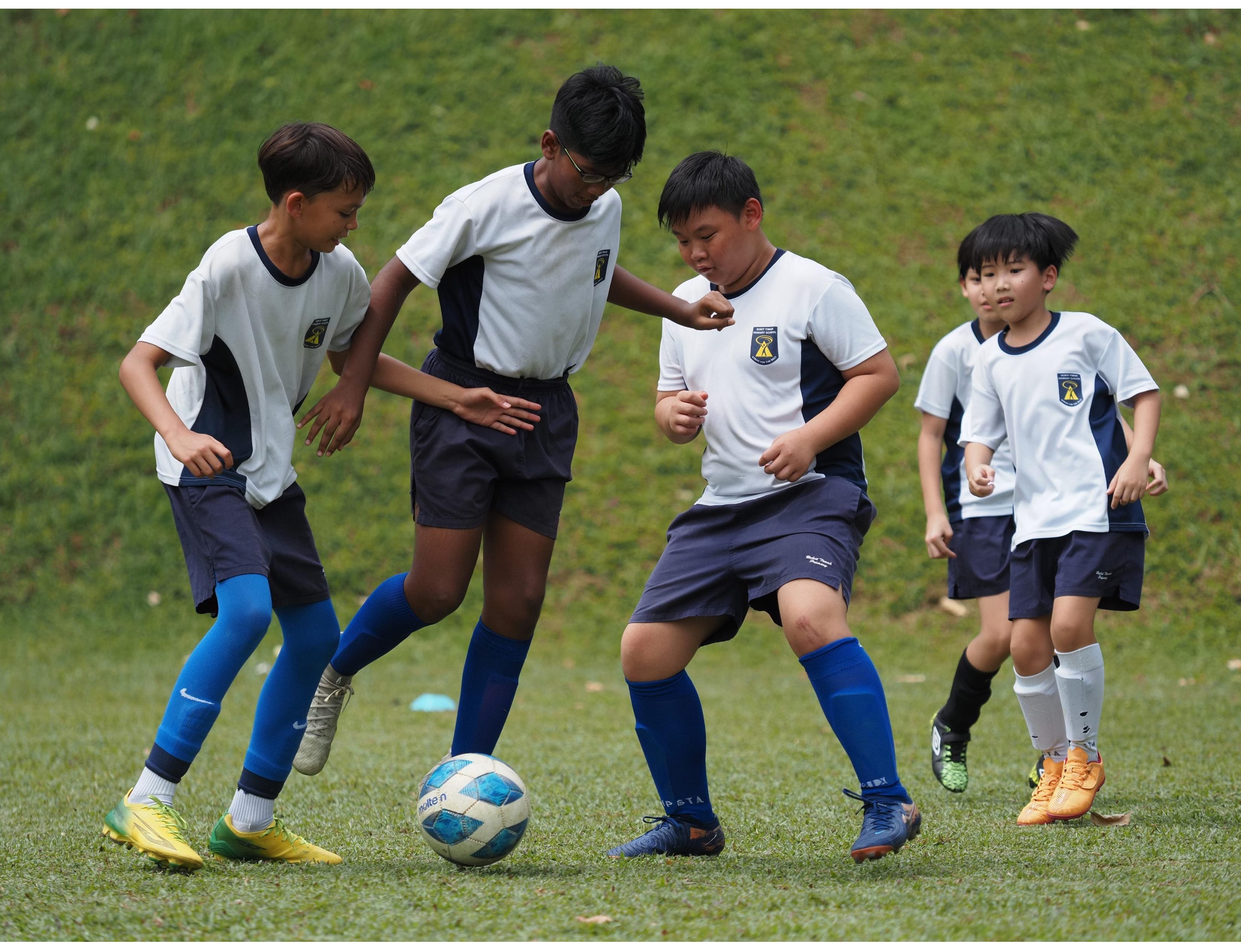 Four boys in matching white and navy uniforms compete for a ball.