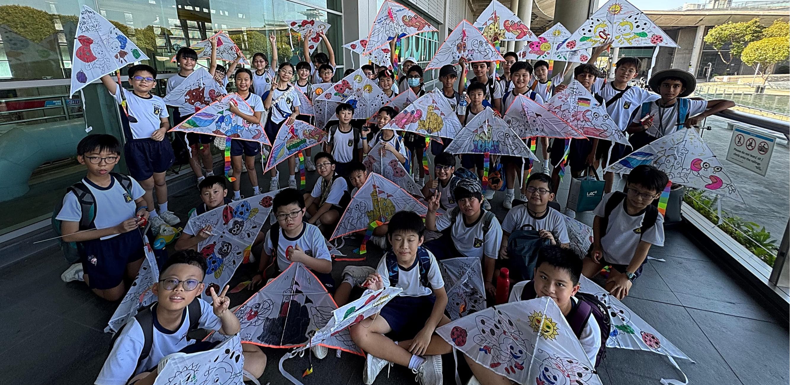 Students display their brightly decorated handmade kites at a sheltered outdoor venue.