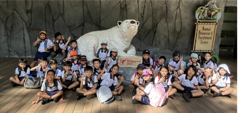 Group of young students in school uniforms posing near a polar bear statue at Singapore Zoo.