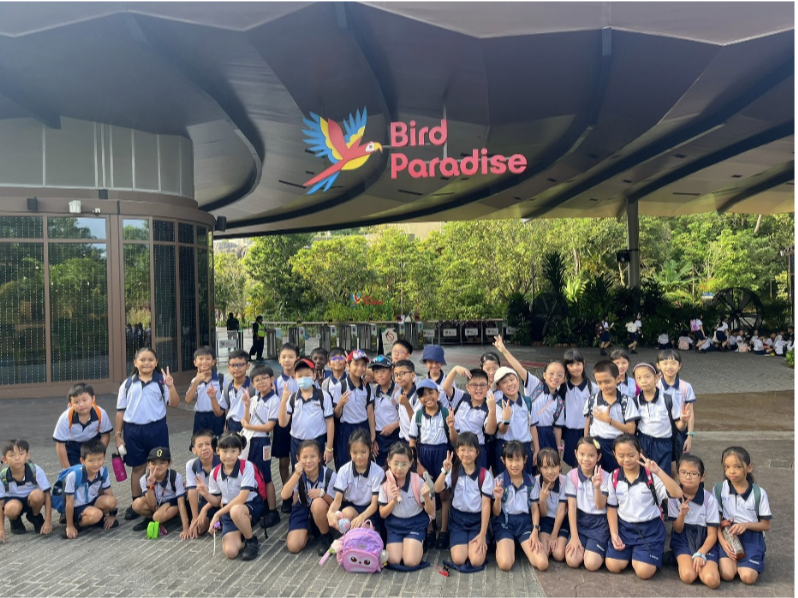 A large group of school children in uniforms posing together at the entrance of Bird Paradise.