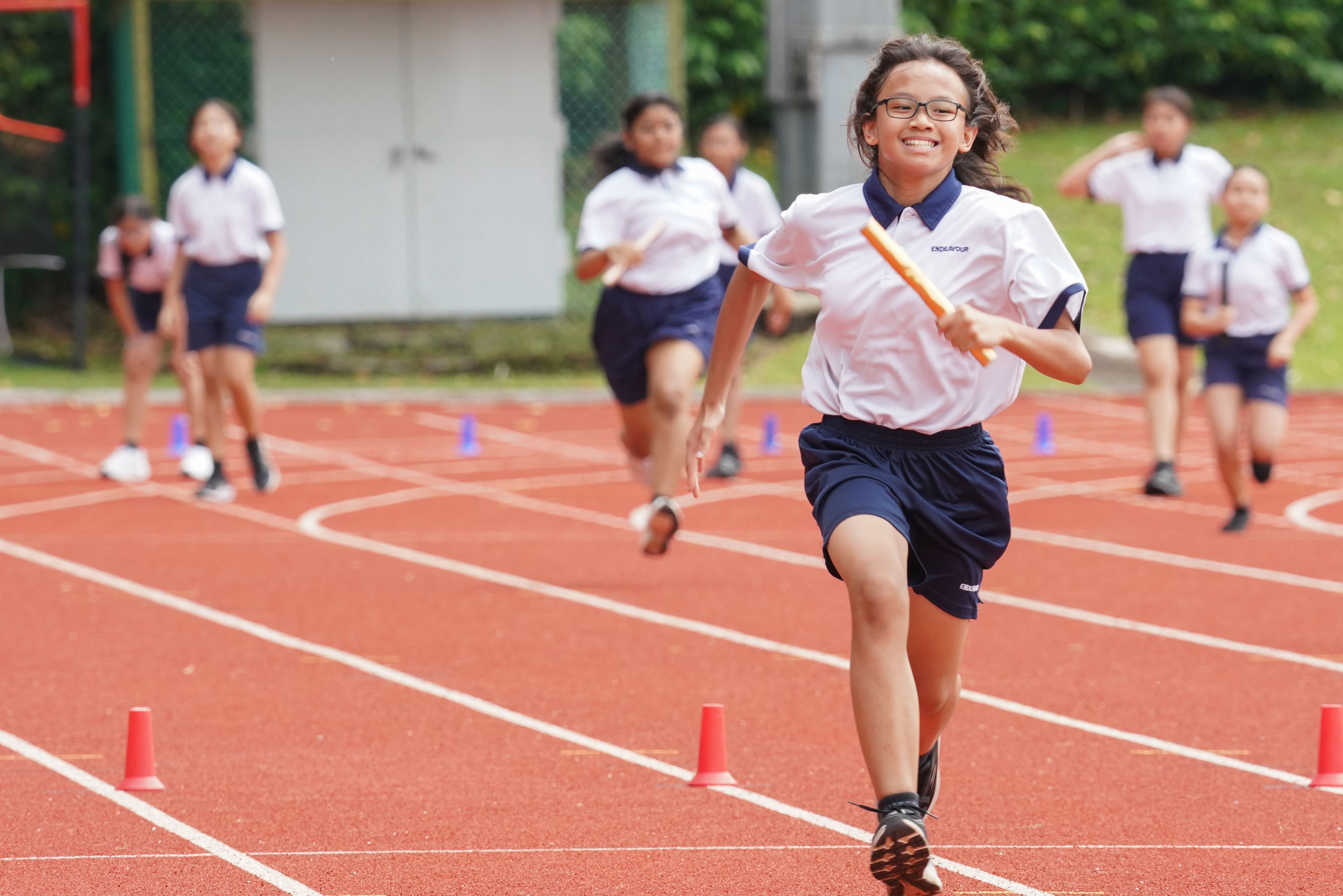 Endeavour Primary School students participating in a relay race on Sports Day, with a student running eagerly across the track holding a baton.