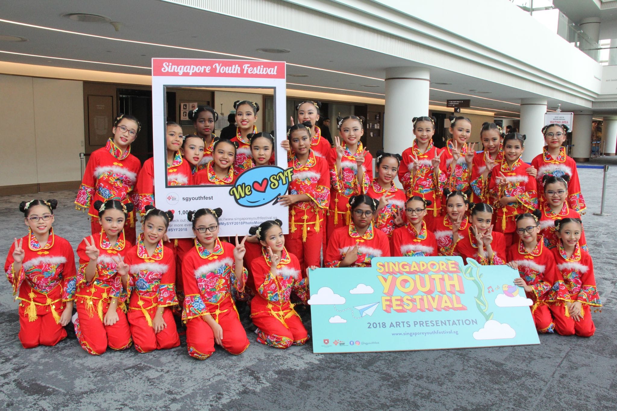 A large group of young girls in red traditional Chinese costumes pose at the 2018 Singapore Youth Festival Arts Presentation.