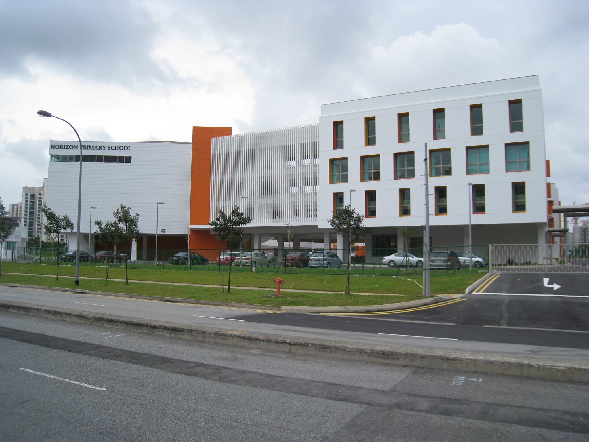 Horizon Primary School, a modern white and orange multi-storey building beside a road with parked cars and a green lawn.