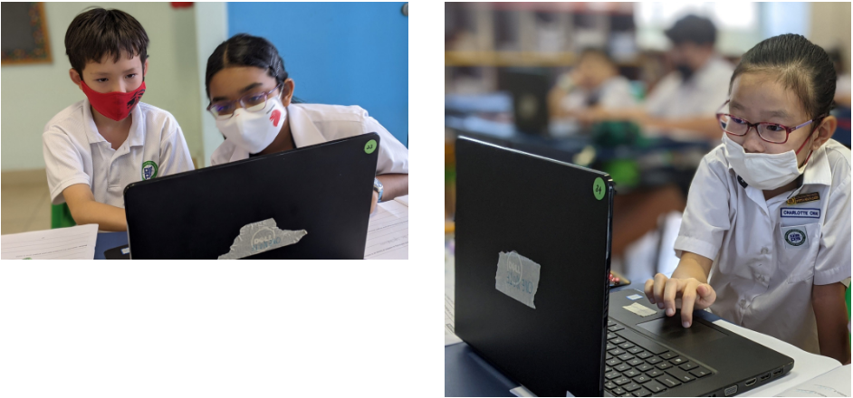 Three masked students in school uniforms work on black laptops in a classroom setting.