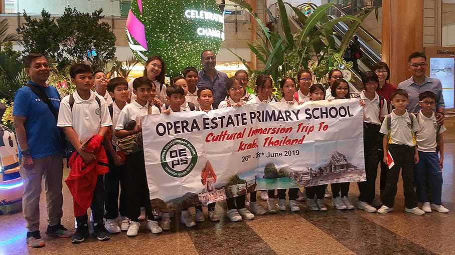 Group of students and adults holding a banner for Opera Estate Primary School Cultural Immersion Trip to Krabi, Thailand, June 2019.