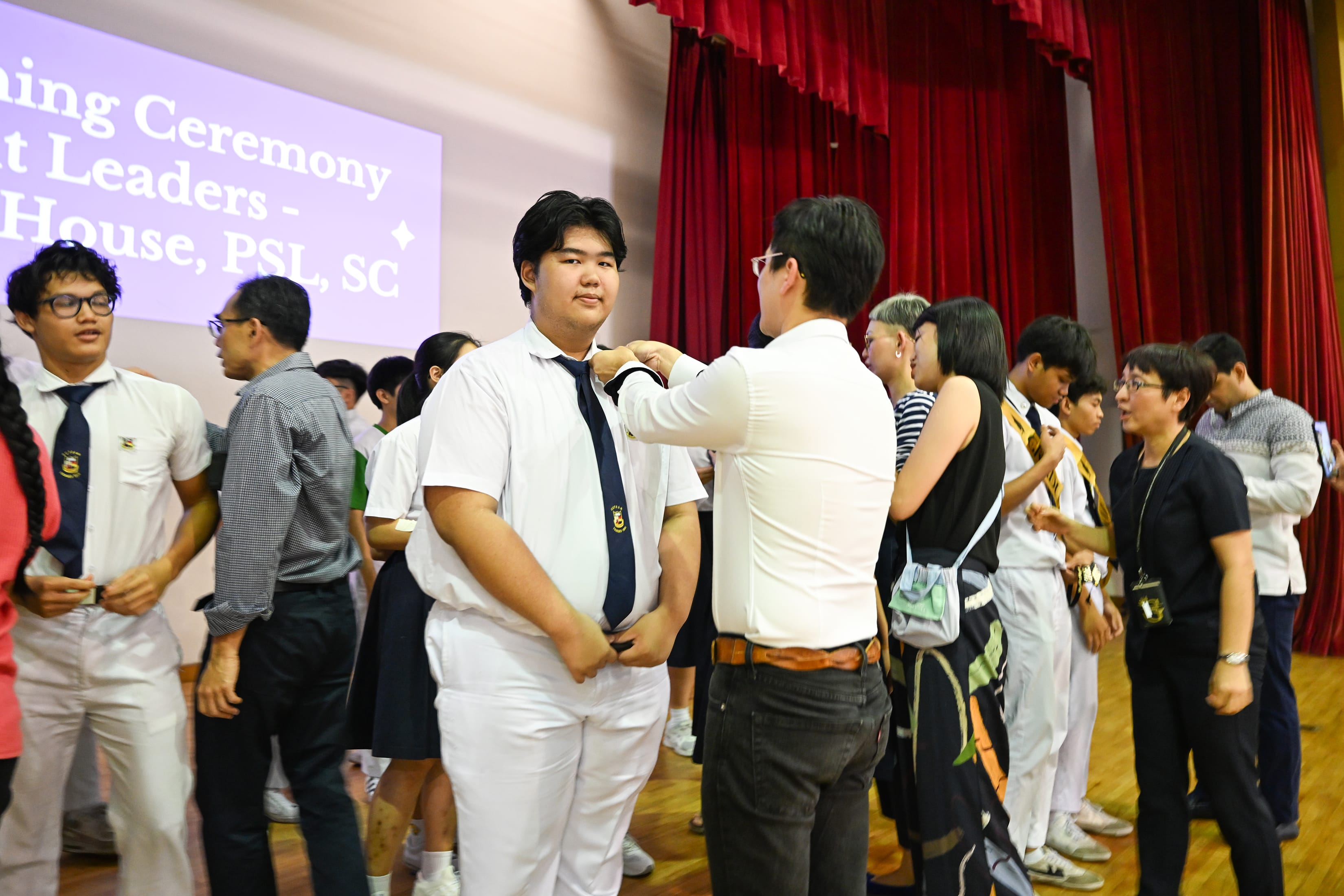 A male in white shirt helping a boy in white uniform wear a badge on his collar.