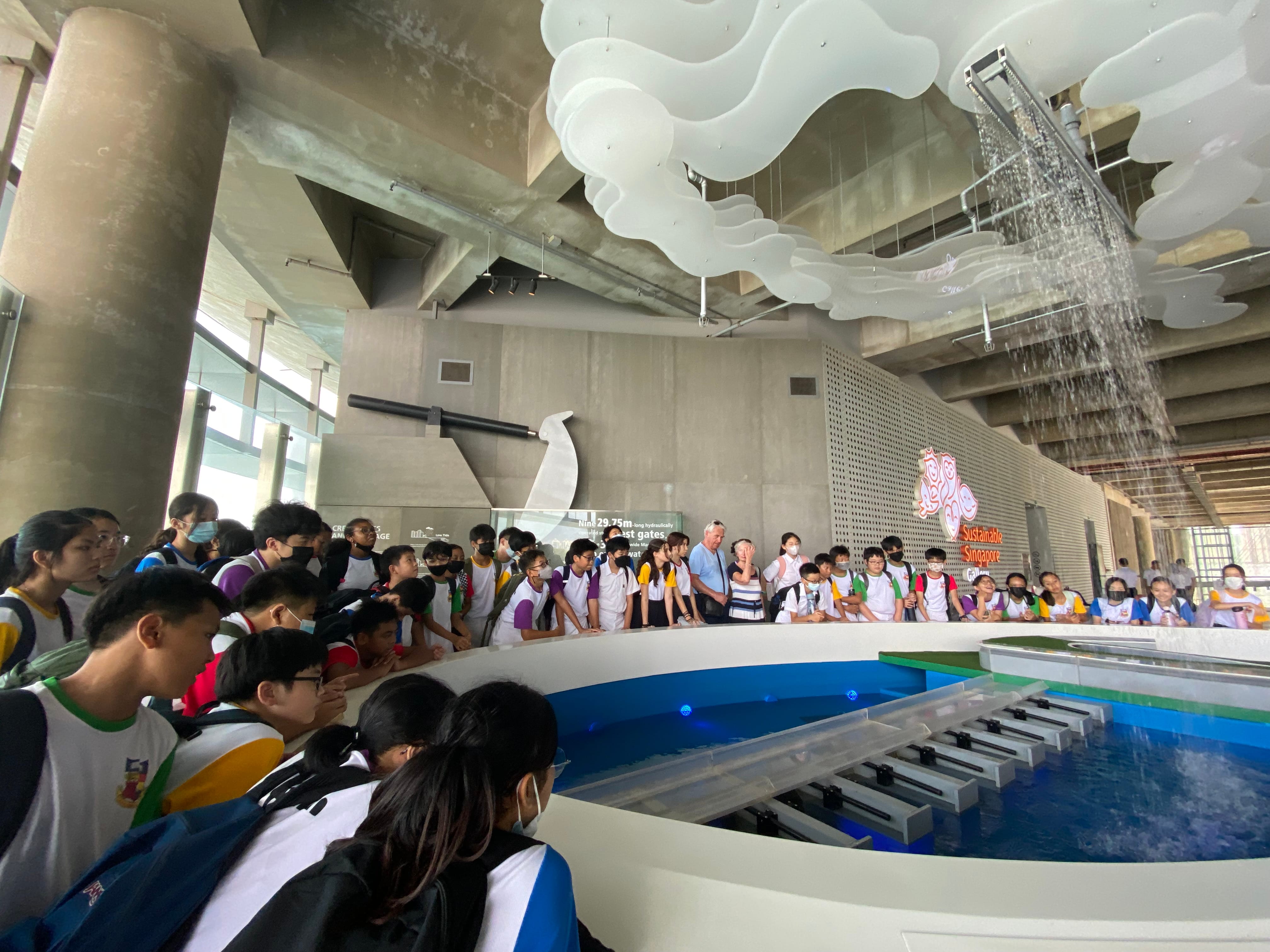 Students gather around a water exhibit at the Sustainable Singapore Gallery, with a waterfall feature above.