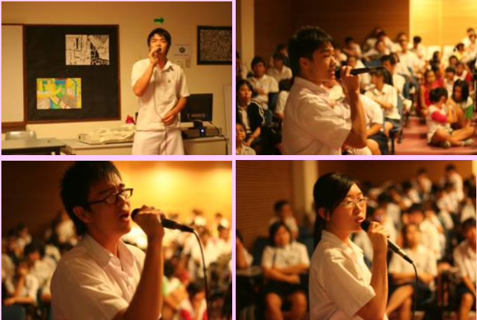 Four students in white shirts sing into microphones at a school event with a seated audience in the background.