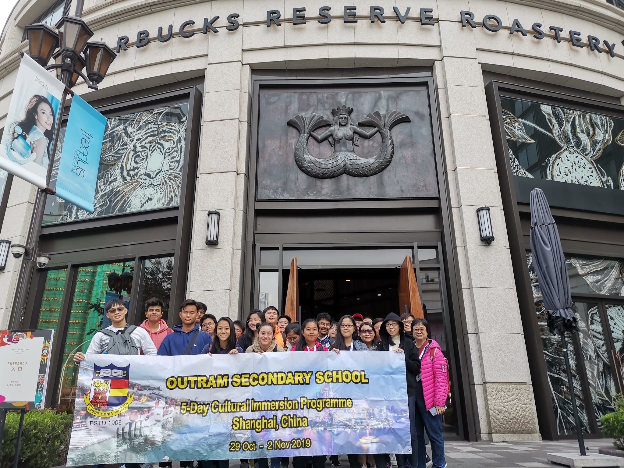 Group of students holding an Outram Secondary School banner outside Starbucks Reserve Roastery in Shanghai, 2019.