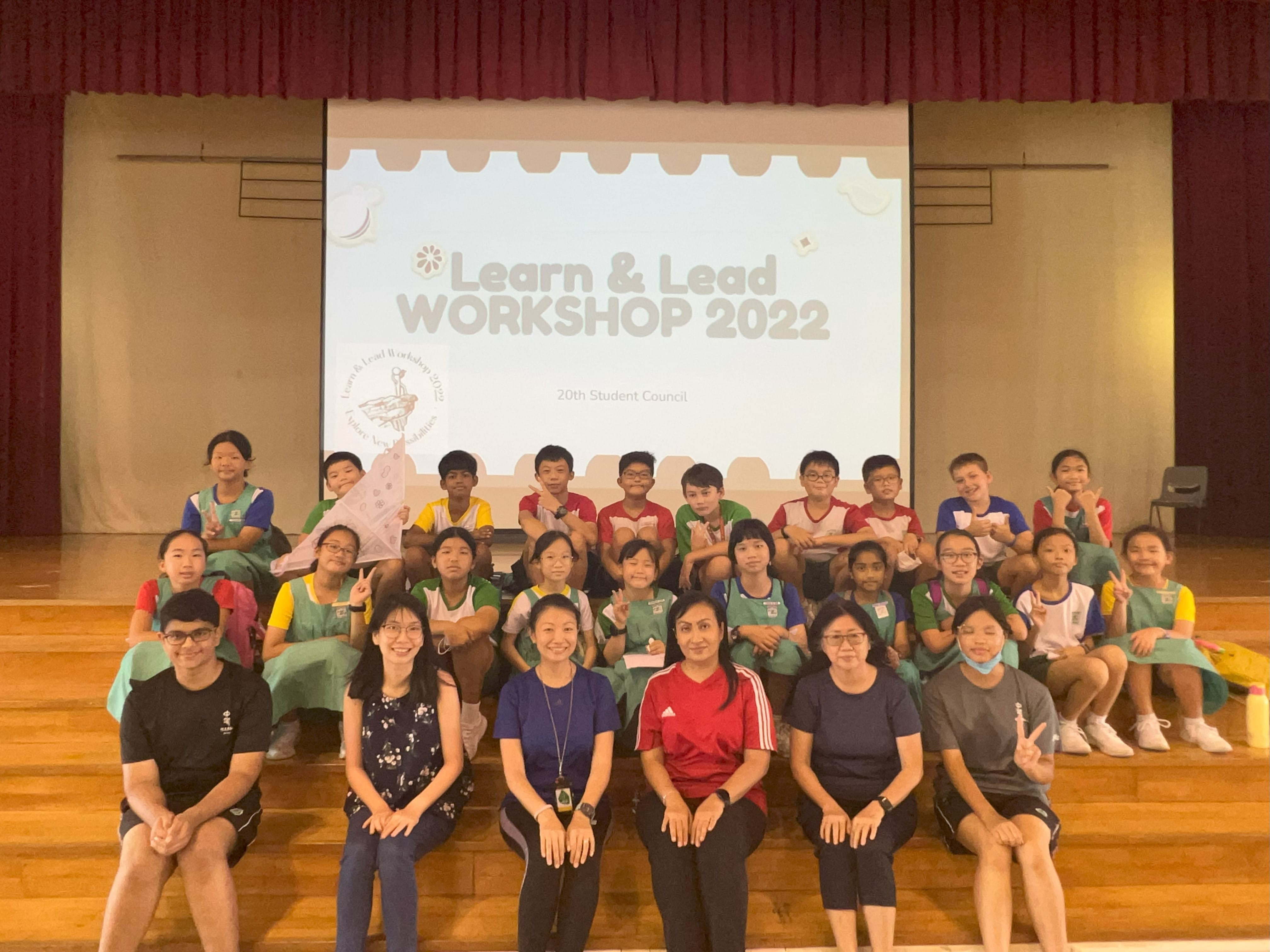 Group of students and teachers posing in a hall before a projected screen reading "Learn & Lead Workshop 2022."