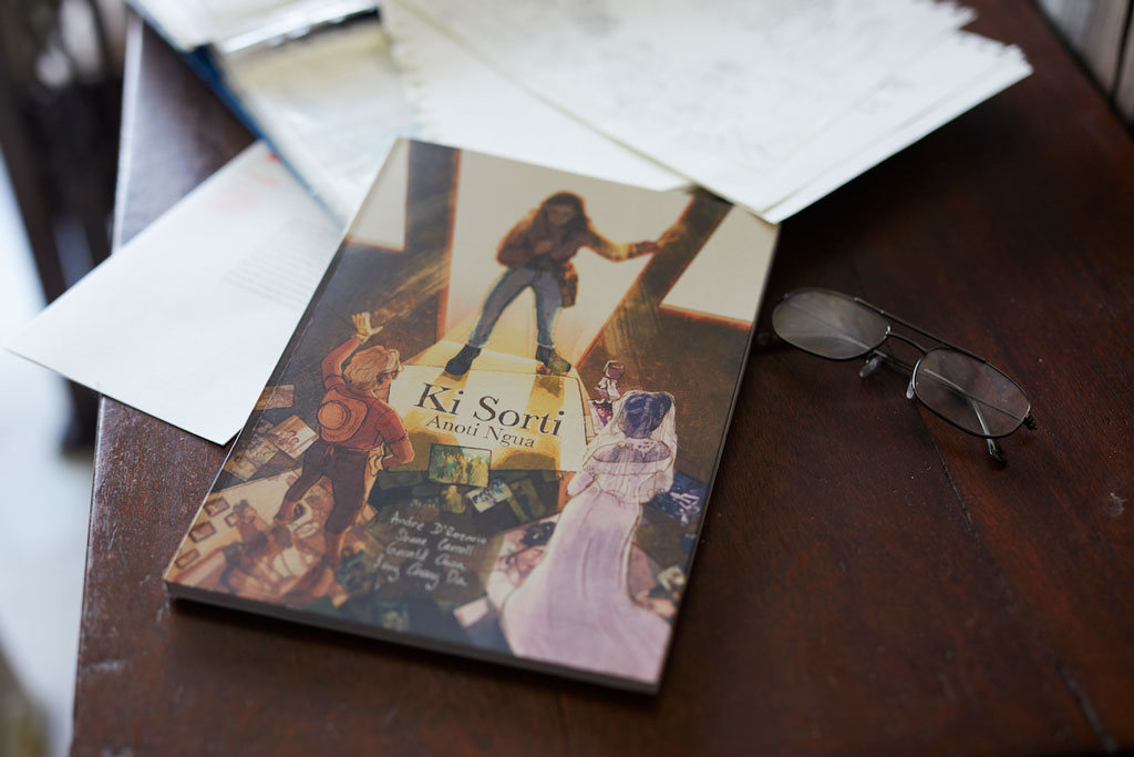 A book titled 'Ki Sorti' by Anoti Ngua placed on a wooden table with eyeglasses beside it.