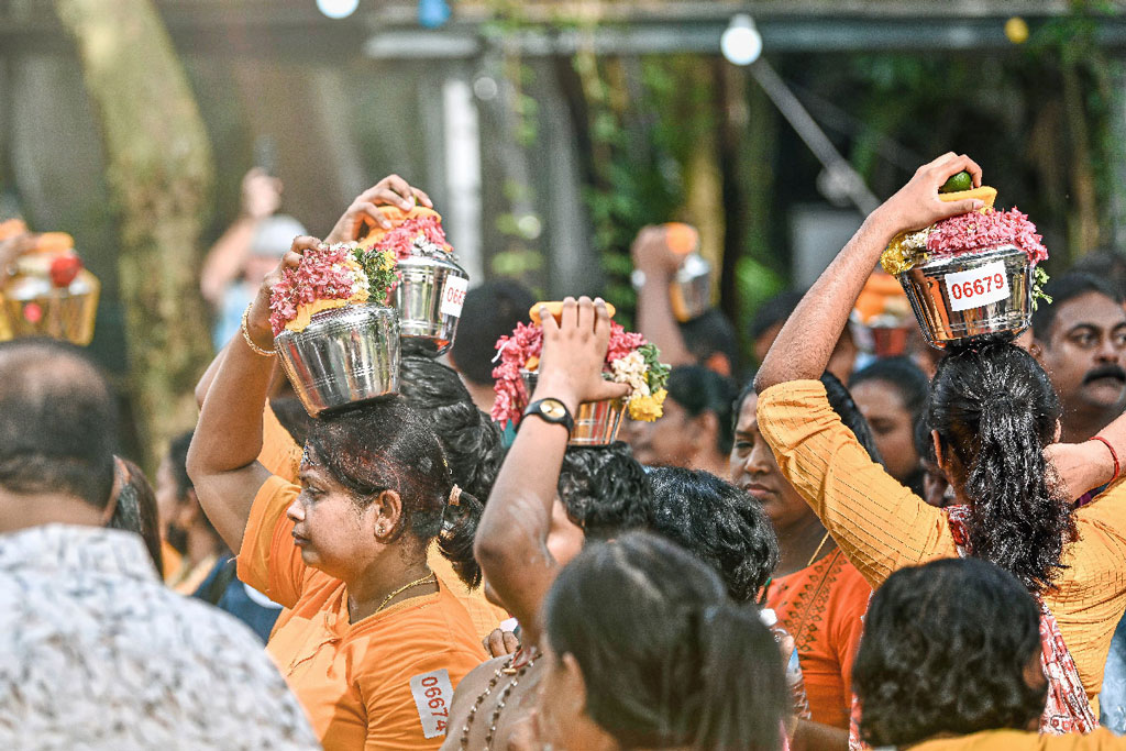 Women carrying decorated silver pots with flowers as offerings during Thaipusam procession.