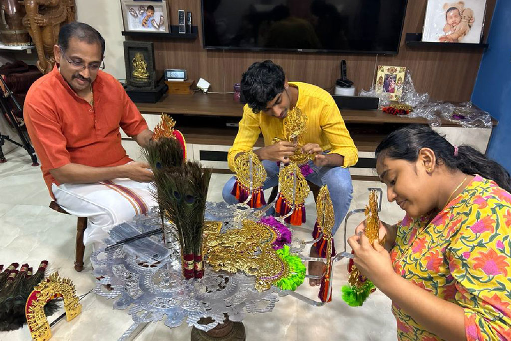 Family working together to decorate kavadi parts with peacock feathers and ornaments.