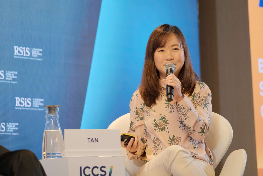 Woman speaking into a microphone while sitting on a panel at an event