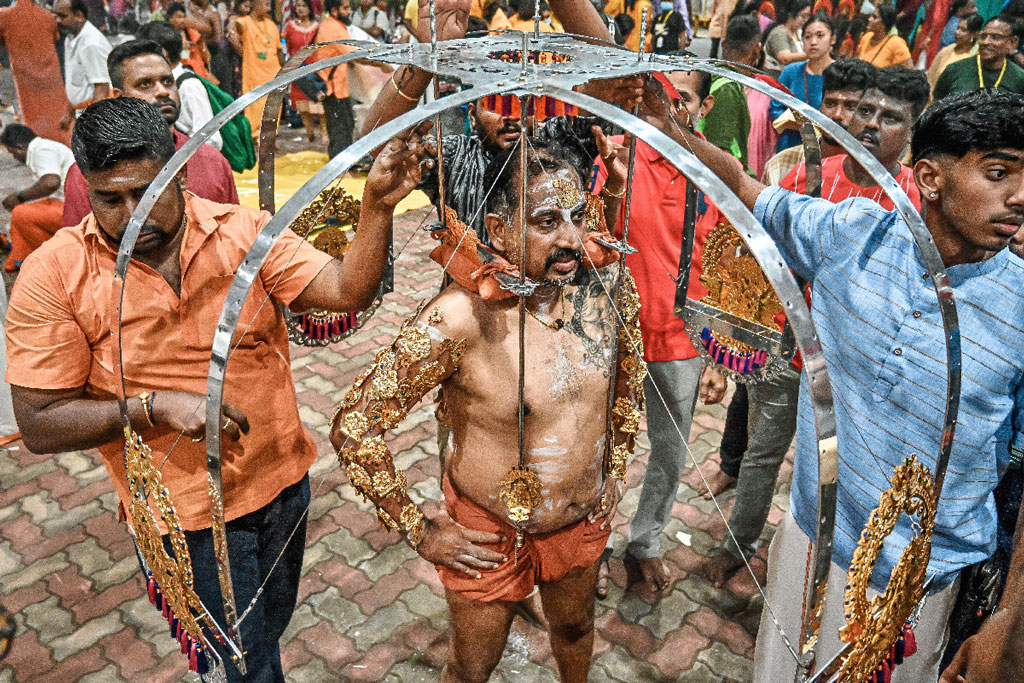 Devotee being helped by others to lift and adjust the kavadi frame during Thaipusam preparations.