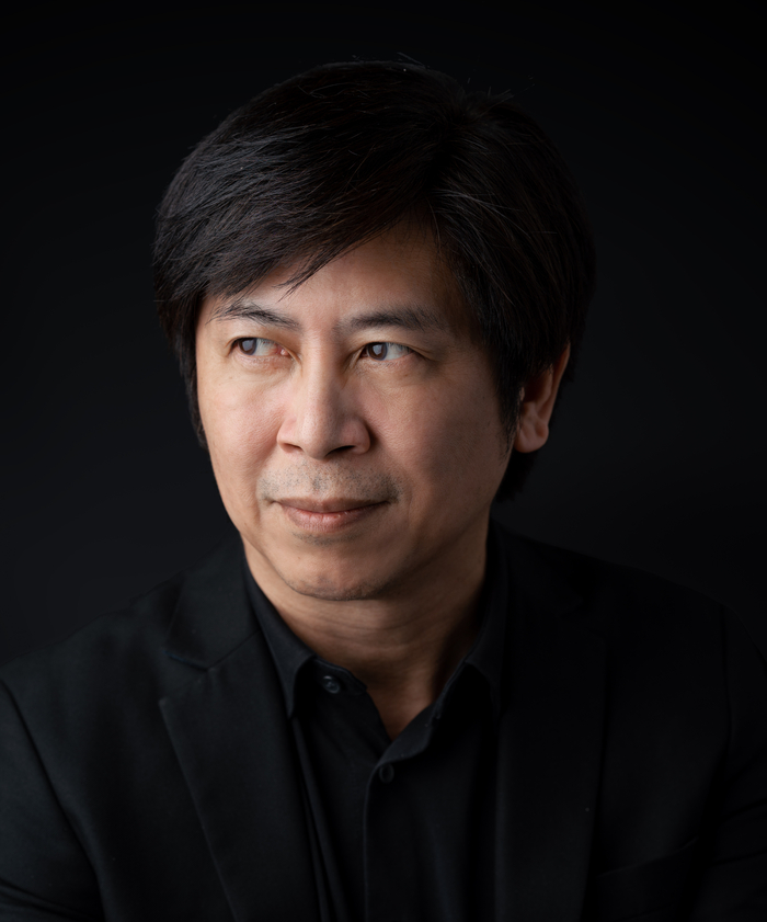 Portrait of a man in a black blazer looking sideways against a dark background.