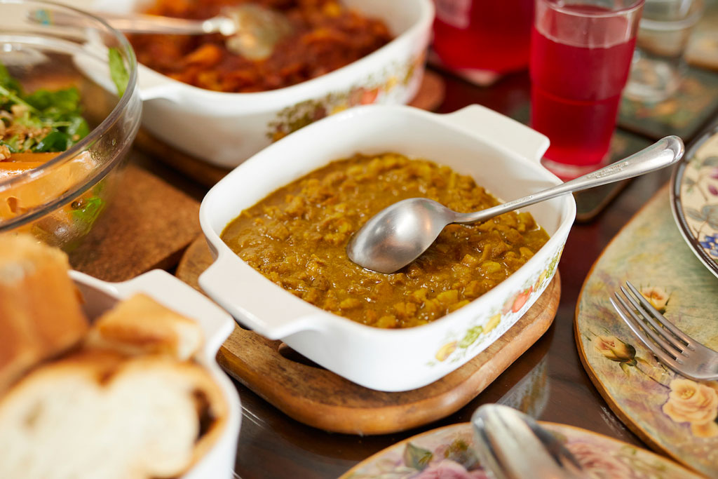Close-up of a dish with curry served in a white bowl, surrounded by bread, salad, and drinks.
