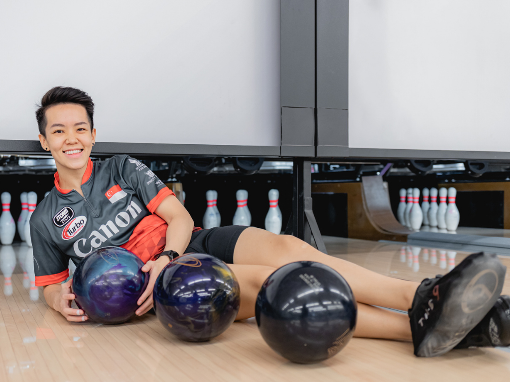 Image of a woman bowling at a bowling alley, wearing a bowling shirt