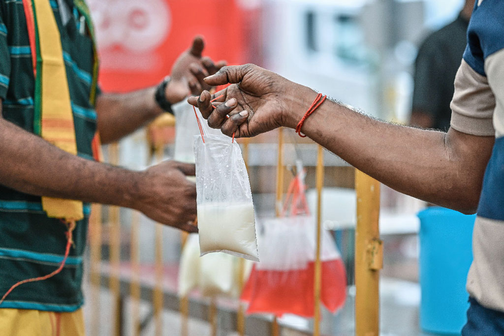 Close-up of a hand holding a plastic bag of milk offered to devotees during Thaipusam.
